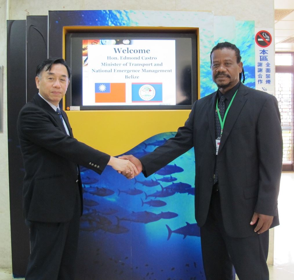 陳所長 (左) 與卡斯卓部長 (右) 於歡迎海報前握手致意